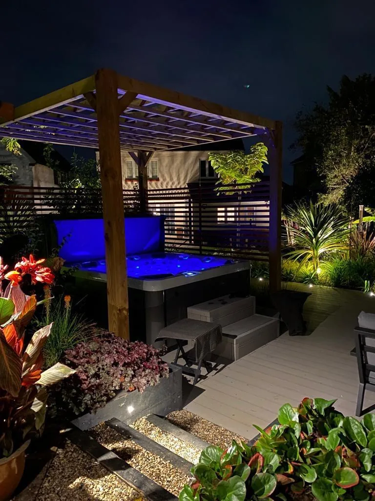 Lit pergola at dusk over composite decking with festoon lighting in a North London garden